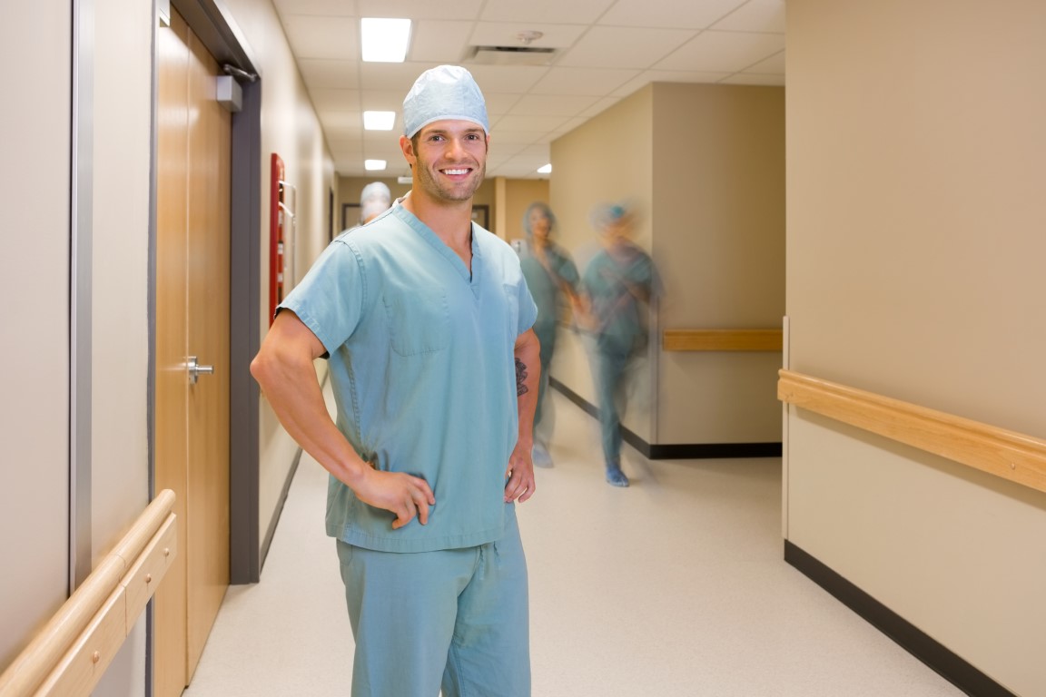 Portrait of confident surgeon with team walking in background at hospital corridor